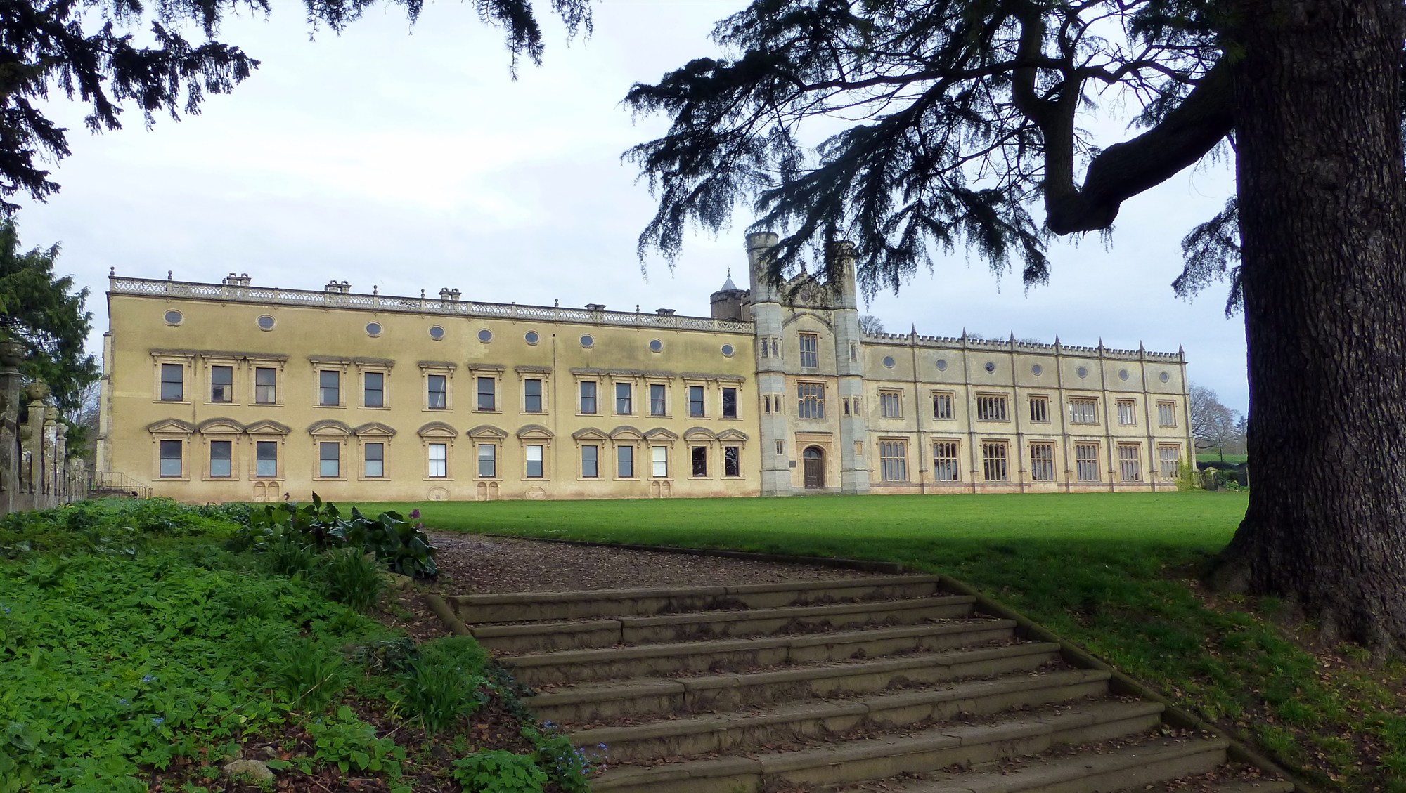 The east elevation of the Manor with its expansive lawn framed by one of the large yew trees that guard it.